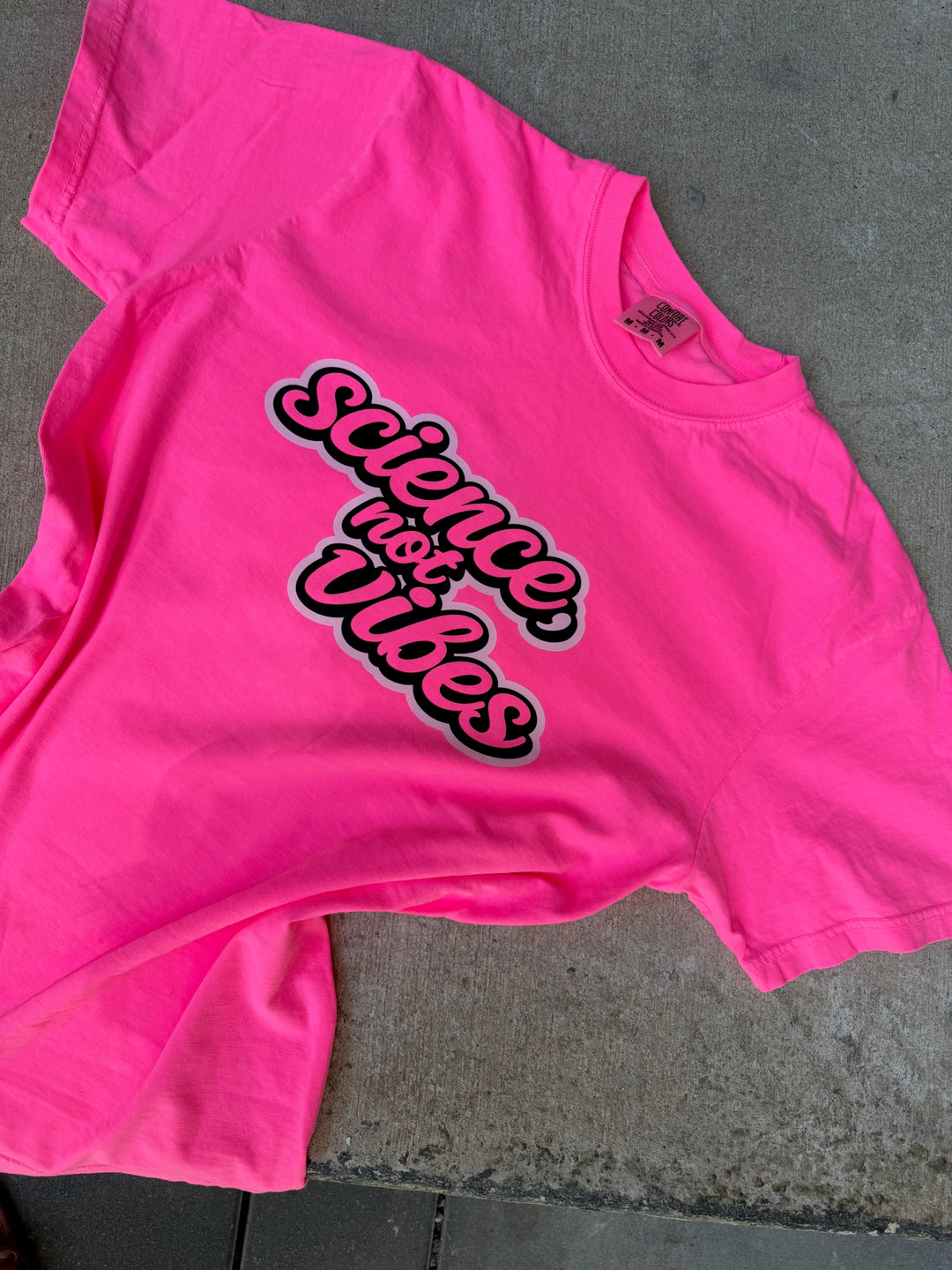 Pink t-shirt with 'Science Vibes' text on a concrete surface