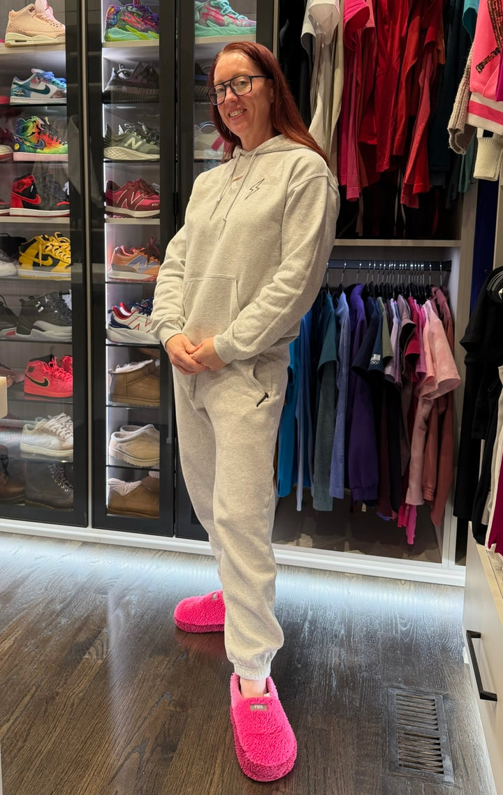 Ladyspinedoc wearing a gray cerebrospinal hoodie and gray pants with pink slippers standing in a room with shelves of shoes and clothes.