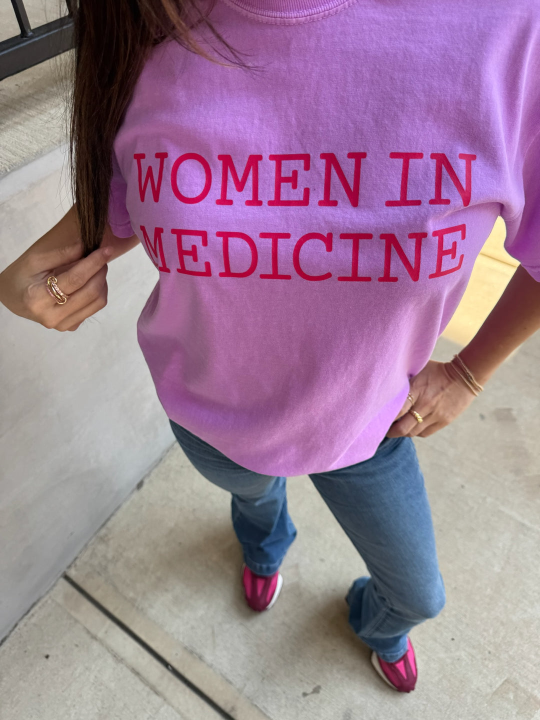 Person wearing a pink 'WOMEN IN MEDICINE' t-shirt indoors.