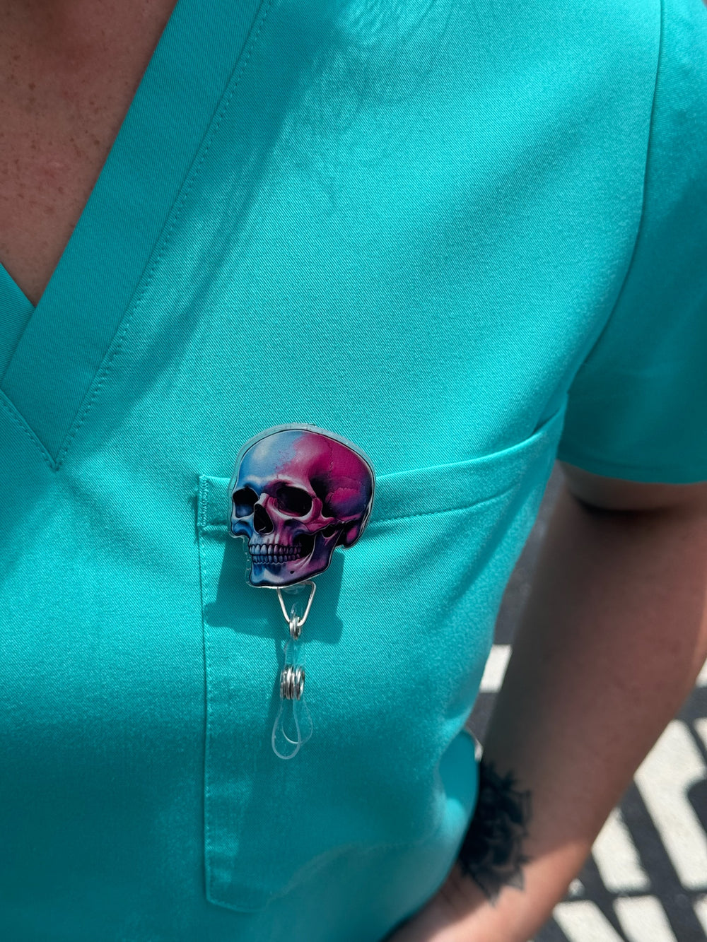 Close up view of Super Skull Badge Reel - Retractable with Alligator Clip and Colorful Skull Design clipped on front pocket of aqua scrub shirt
