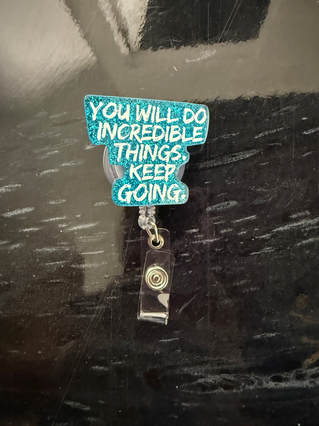 Blue glitter badge reel with "You Will Do Incredible Things. Keep Going." motivational quote in white brush font.