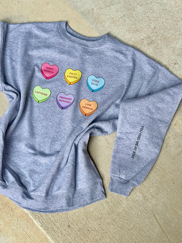 Gray sweatshirt with colorful heart-shaped text on a beige surface