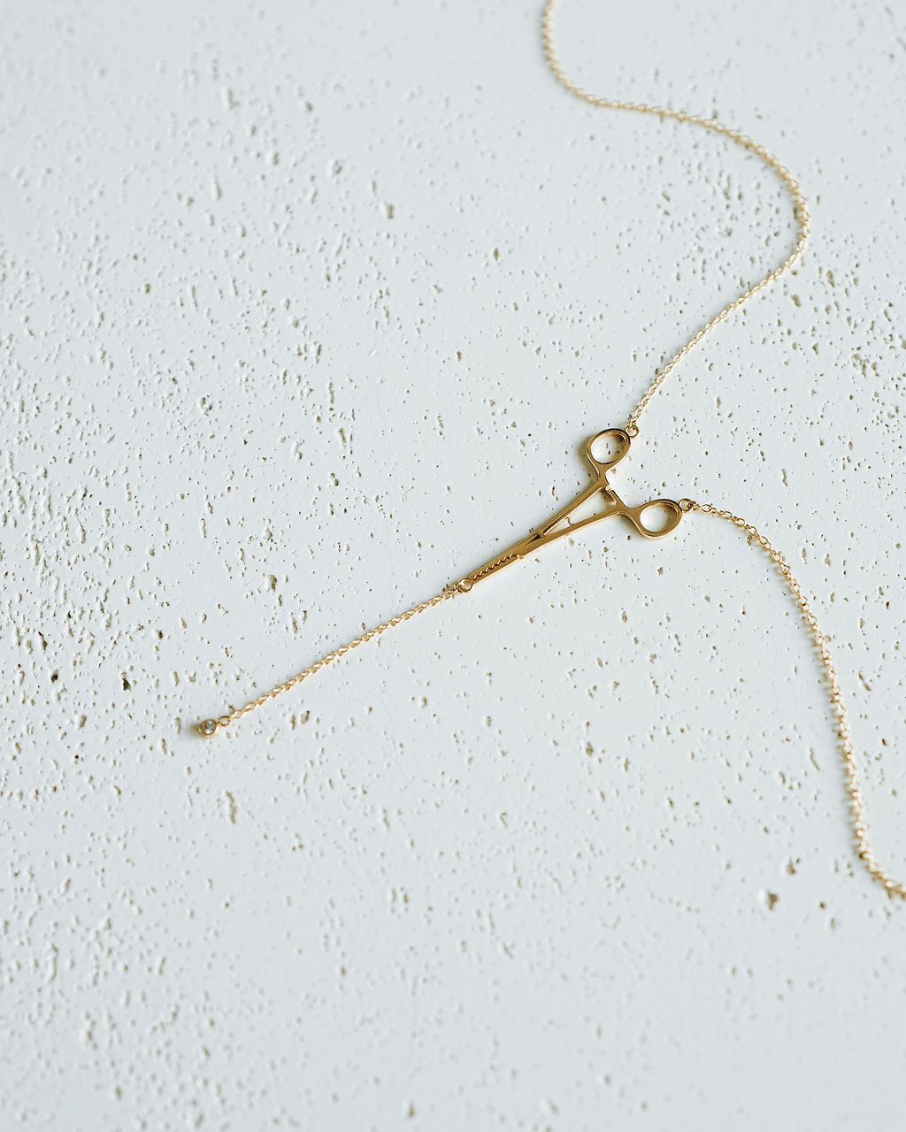 Flat lay of gold Erin Necklace: Hemostat With Diamond Drop