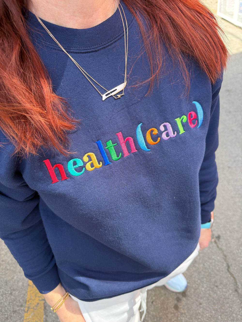 Ladyspinedoc wearing a navy blue sweatshirt with health(care) in colorful letters.