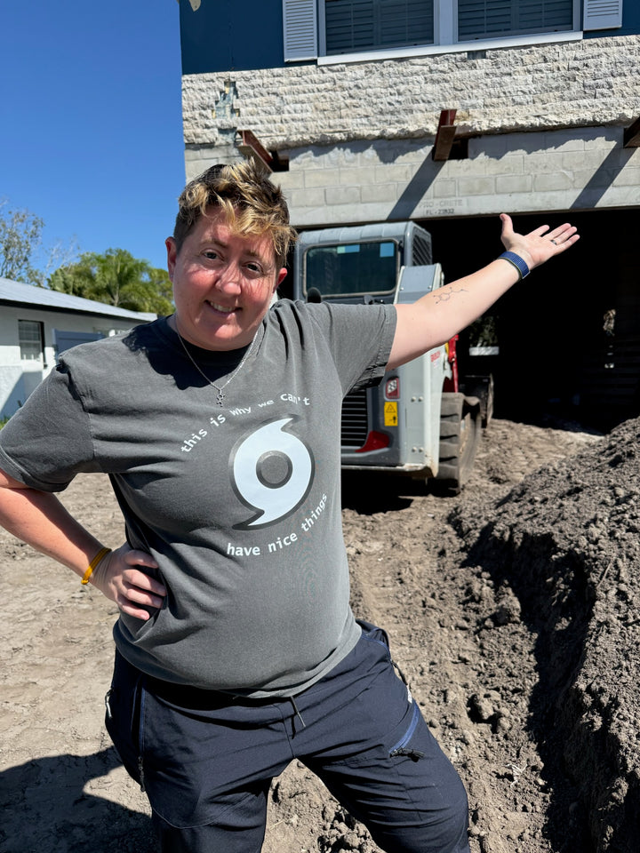 Dr. Beachgem standing in front of her house wearing a gray tee shirt that says "This is why we can't have nice things" with a hurricane symbol