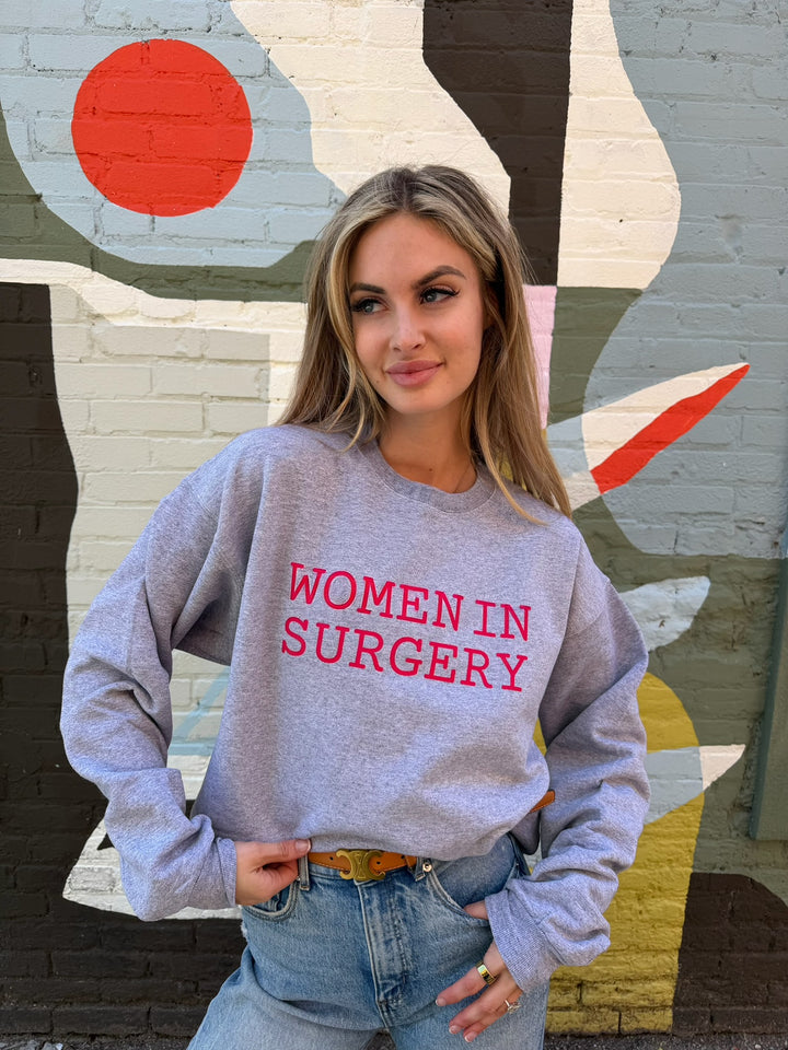 Woman wearing a gray sweatshirt with 'Women in Surgery' text in front of a colorful mural.