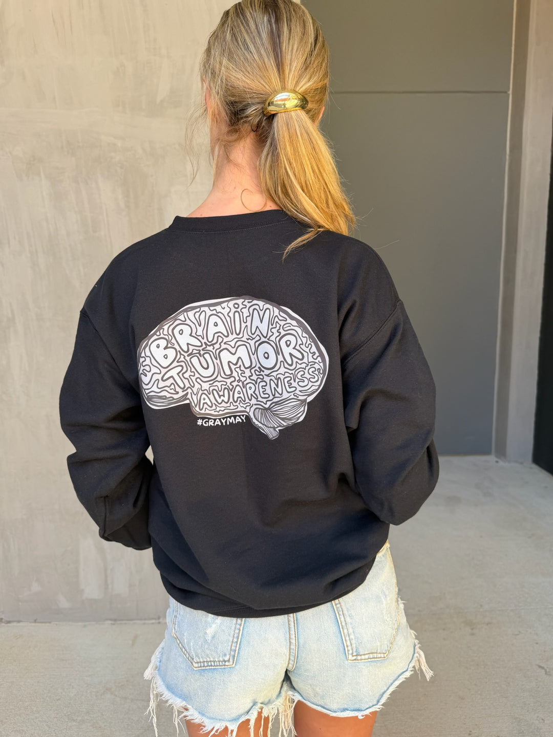 Person wearing a black sweatshirt with a graphic design on the back, standing against a neutral wall.