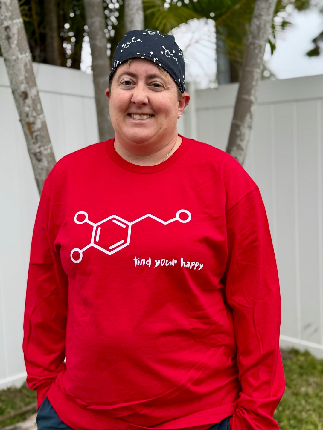 Dr. Beachgem wearing a red long sleeve t-shirt with a dopamine chemical structure design and Find Your Happy text, standing outdoors.