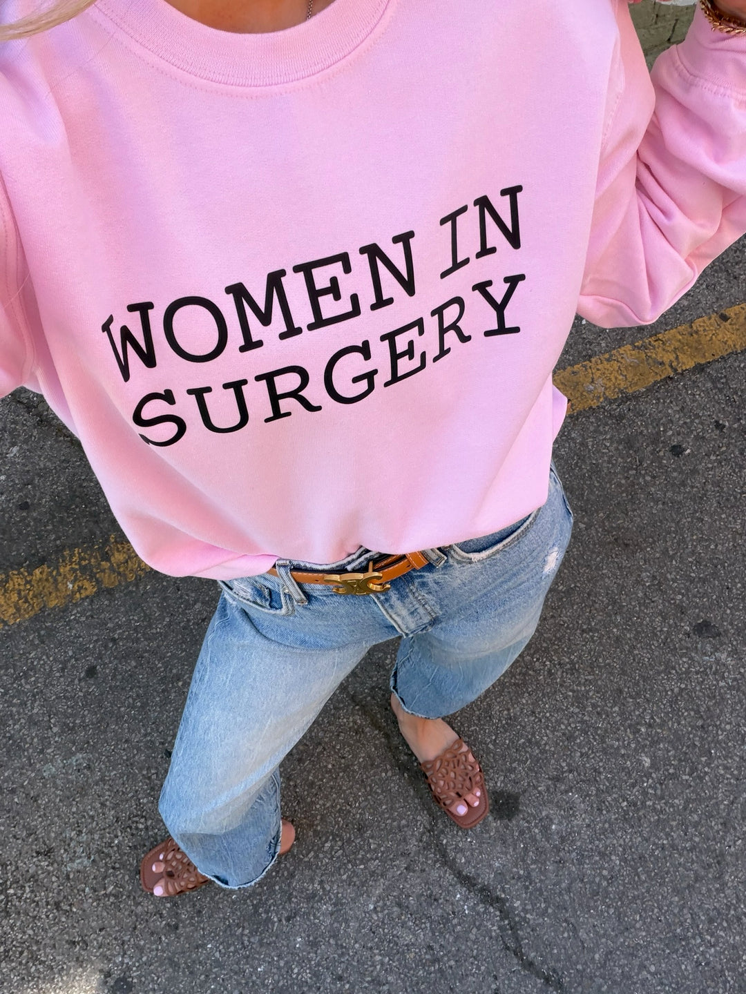 Person wearing a pink shirt with 'WOMEN IN SURGERY' text on a pavement background