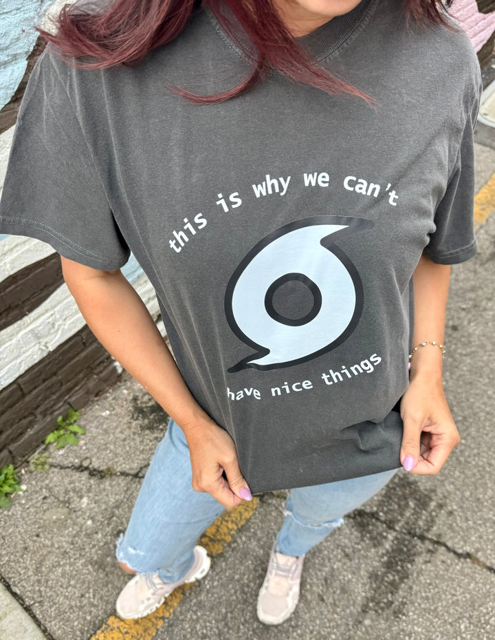 Person wearing a dark gray t-shirt with a storm graphic and this is why we can't have nice things text on a pavement background