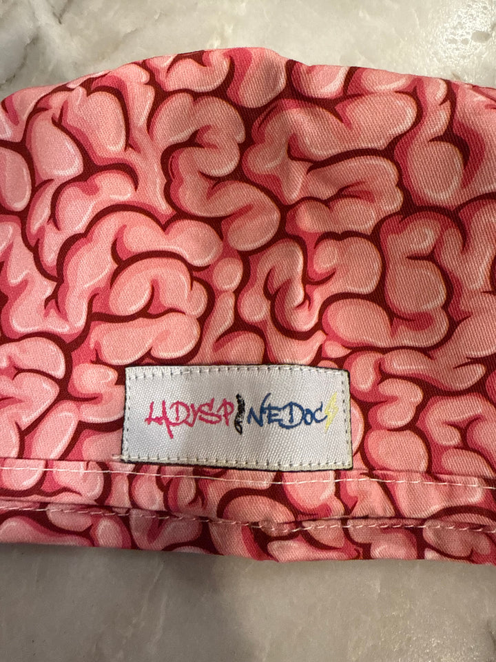 Close up of the brain print and Ladyspinedoc logo tag sewn on the outer side of the pink Cortex Scrub Hat