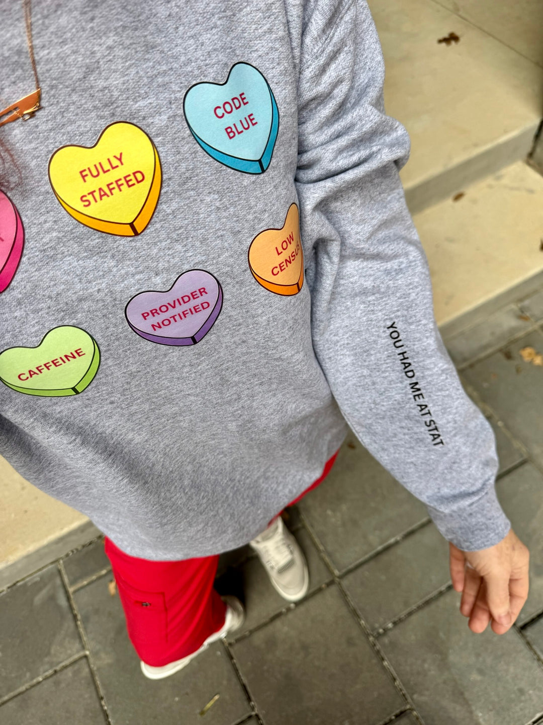 Gray sweatshirt with colorful heart-shaped graphic and You Had Me At Stat on sleeve on Ladyspinedoc outdoors.