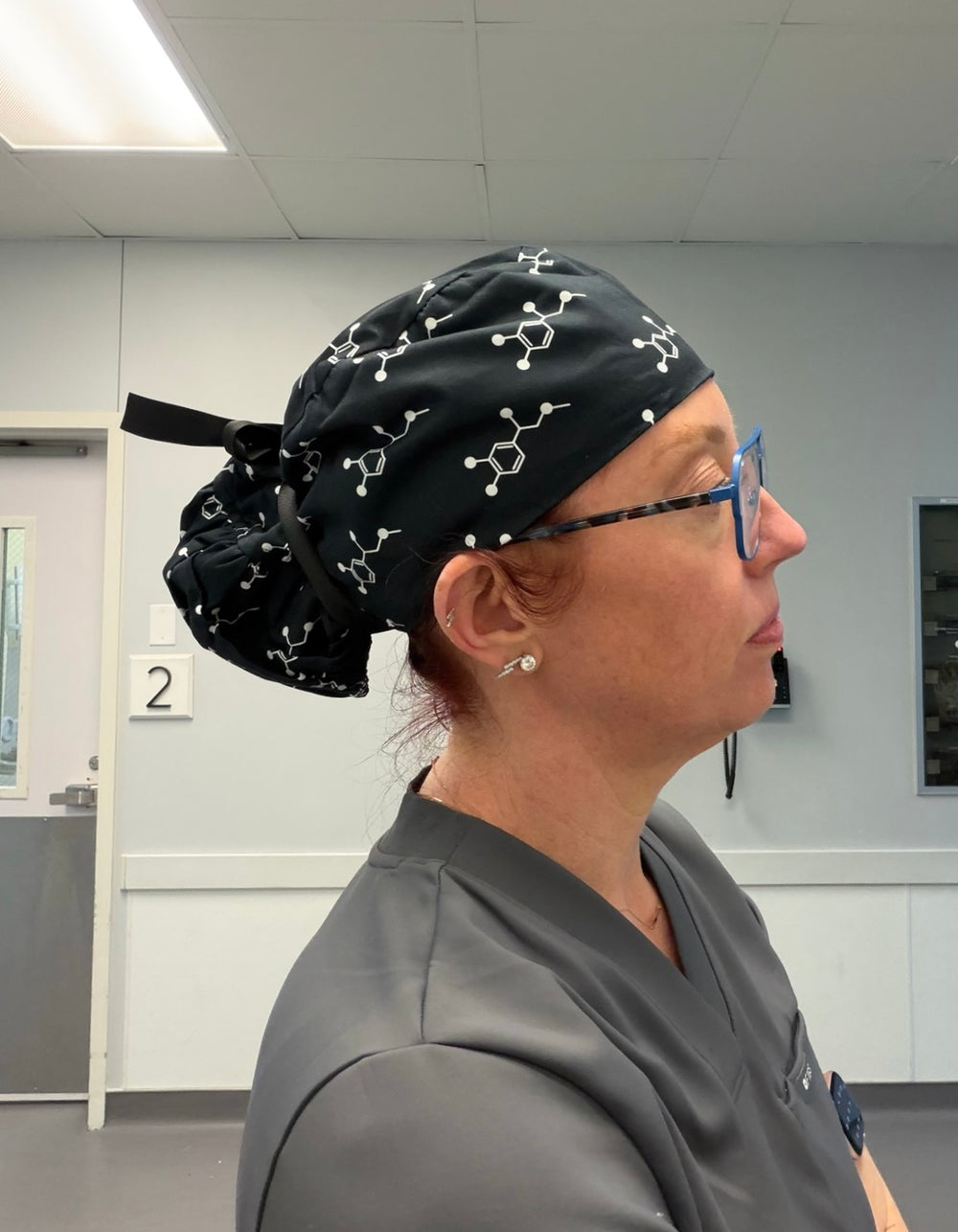 Ladyspinedoc wearing a black scrub cap with molecular designs in a medical setting.