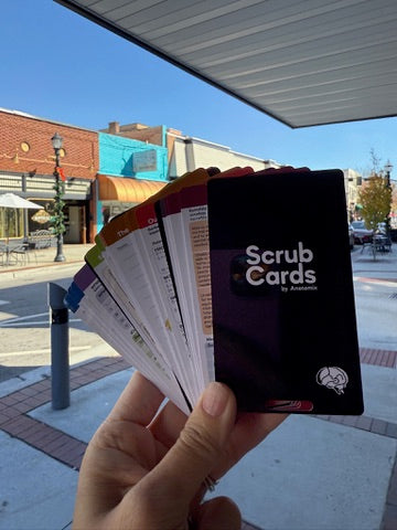 Hand holding a pack of 'Scrub Cards' with a city street in the background