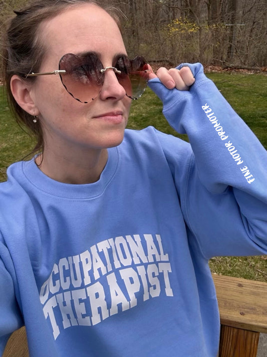 OT Lindsay DeLong wearing a blue Occupational Therapist sweatshirt (designed by Ladyspinedoc) and showing off the "Fine Motor Promoter" motto on the left sleeve. 