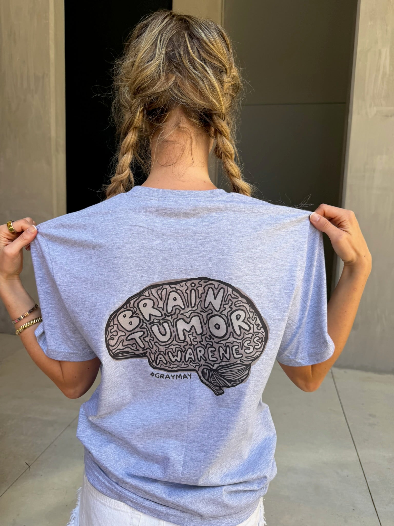 Person wearing a light gray t-shirt with a brain tumor awareness design on the back.