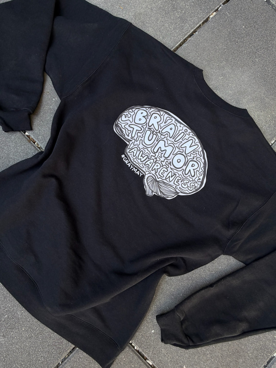 Black sweatshirt with white Brain Tumor Awareness graphic design on a gray pavement