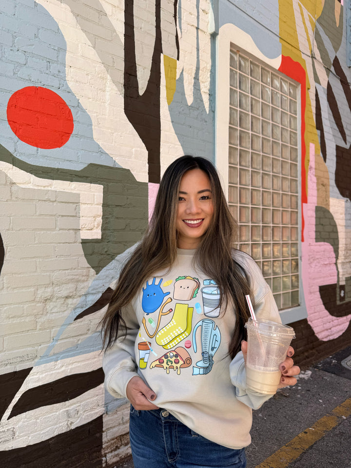 Women wearing a beige Nurse Sweatshirt with cartoon nurse memorabilia on the front. 