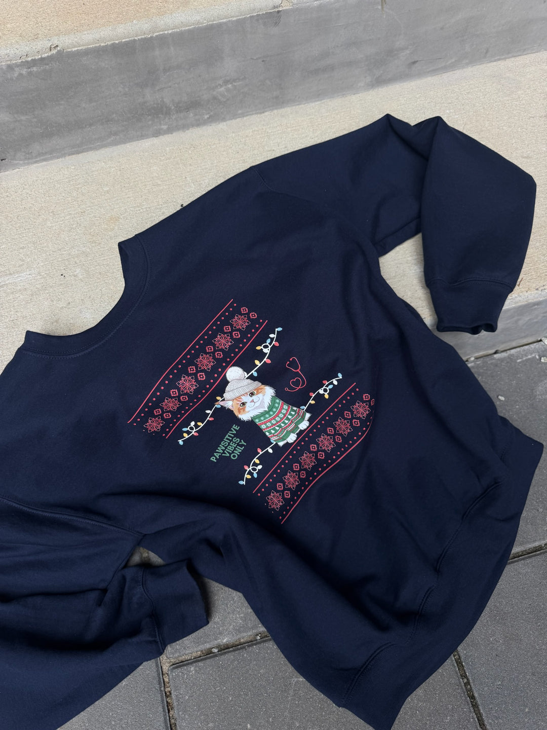 Navy blue sweatshirt with a Christmas cat design on a concrete surface