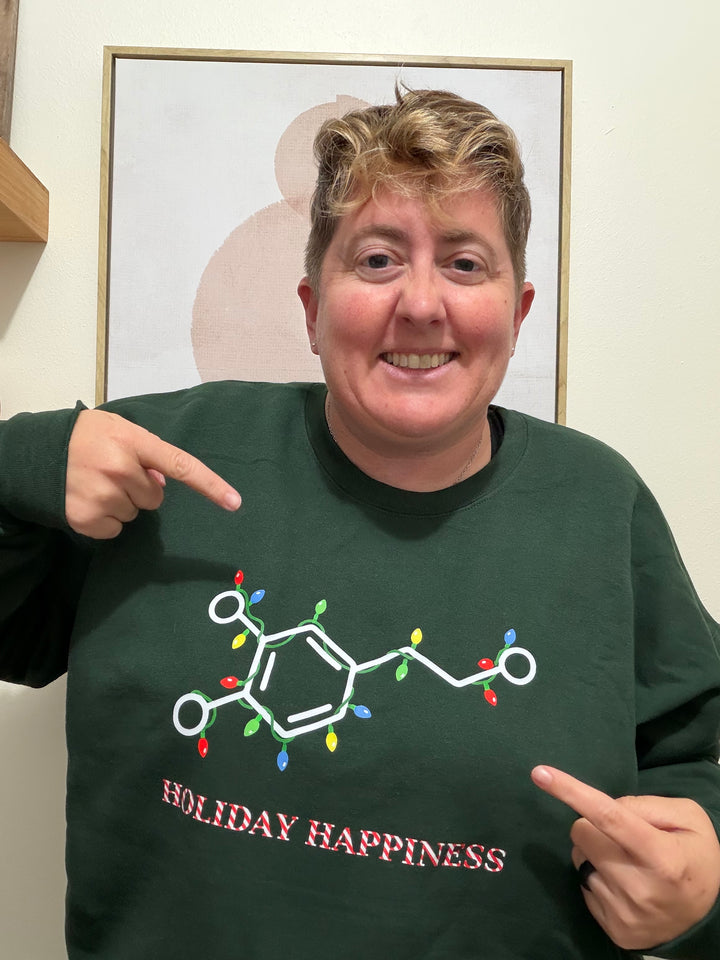 Dr. Beachgem wearing a green sweatshirt with 'Holiday Happiness' molecule design, pointing at the text.