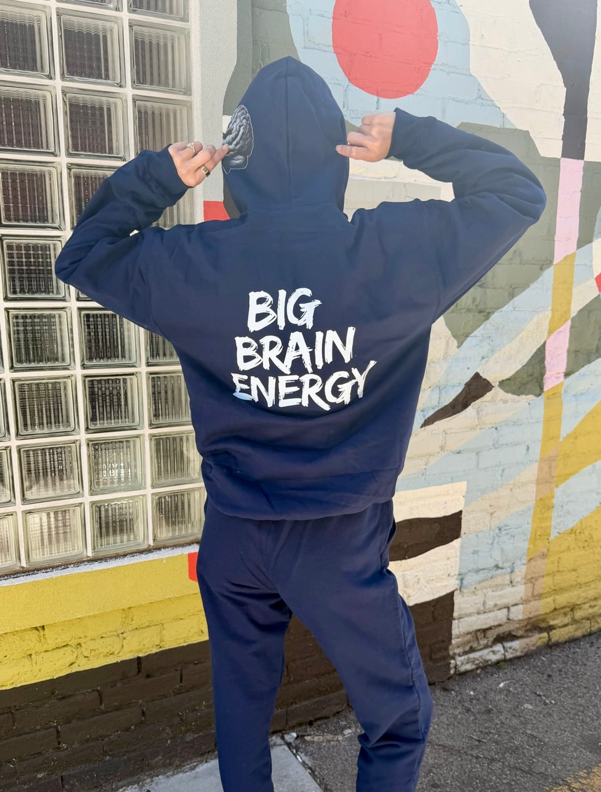 Person wearing a navy blue hoodie with 'BIG BRAIN ENERGY' text, standing in front of a colorful mural.