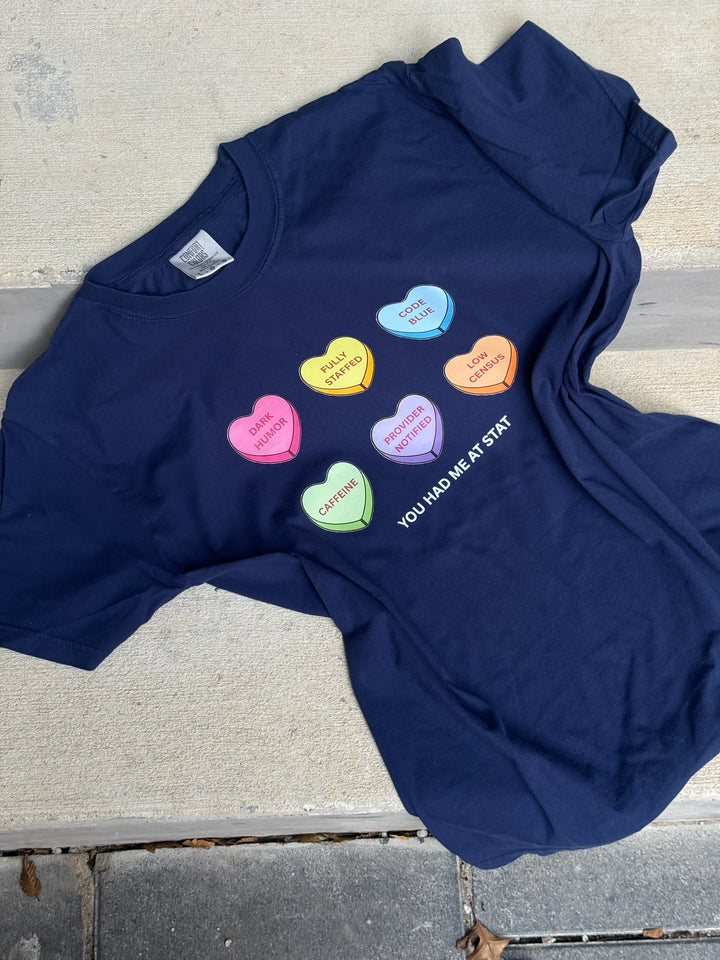 Flat lay of Navy Nurse Tee with Candy Hearts design and You Had Me At Stat text on a concrete surface