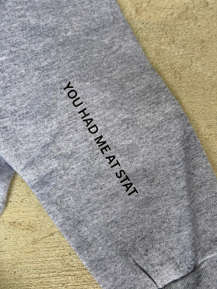 Gray sweatshirt with text 'YOU HAD ME AT STAT' on a beige surface
