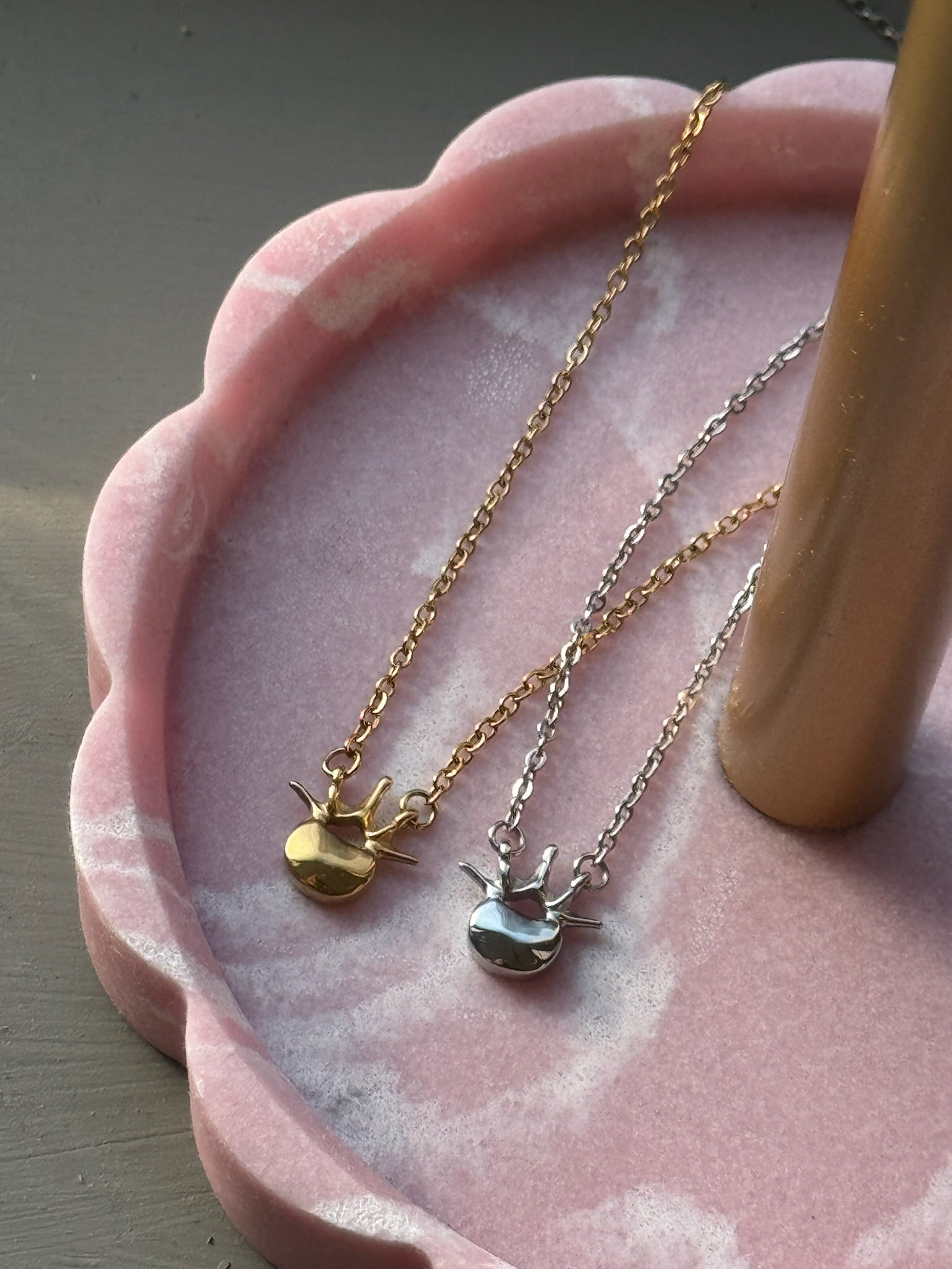 Ladyspinedoc Lumbar Spine Vertebra Necklaces in Silver and Gold in a pink and white scalloped tray.