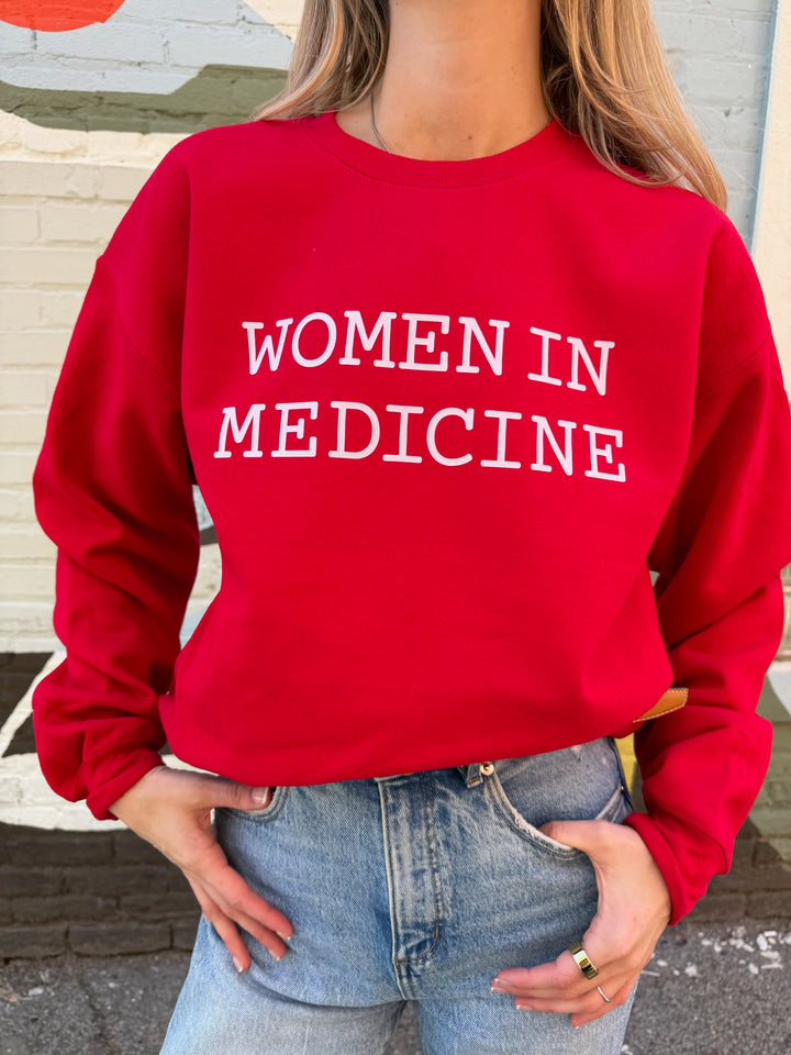 Person wearing a red sweatshirt with 'WOMEN IN MEDICINE' white text.