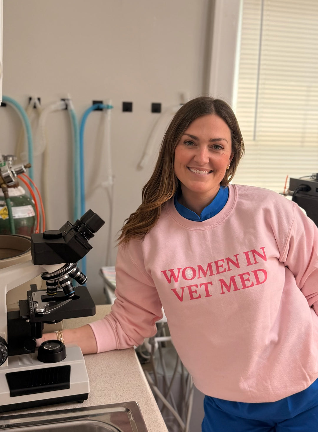 Dr Molly Brinkmann wearing a pink 'Women in Vet Med' sweatshirt in a laboratory setting.