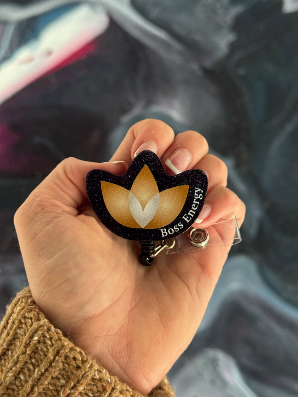 Lotus-shaped keychain with 'Boss Energy' text held in a hand against a blurred background