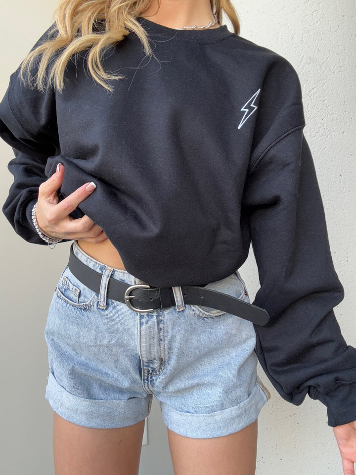 Model wearing The Incredible Sweatshirt, showcasing front lightning bolt detail and holding up the bottom hem on one side. 