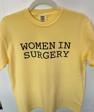 Yellow t-shirt with 'WOMEN IN SURGERY' text on a hanger.
