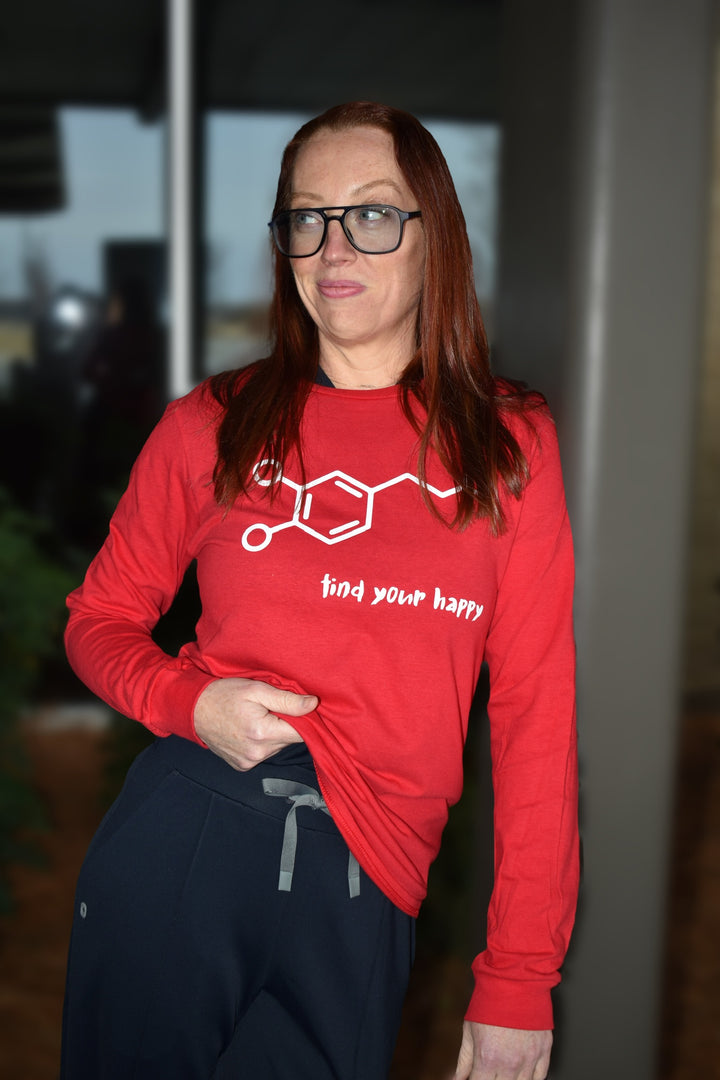 Dr. Betsy Grunch - Ladyspinedoc - holding the hem of her red long-sleeve t-shirt that features a white dopamine molecule on the front with the phrase “find your happy” below in a playful brush font.