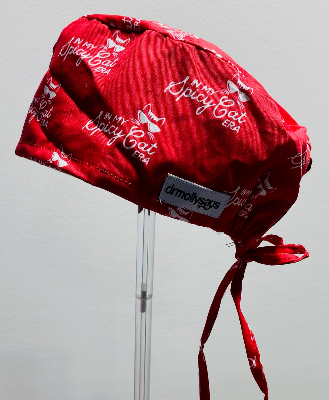 Red scrub cap with 'In My Spicy Cat Era' text on a gray background