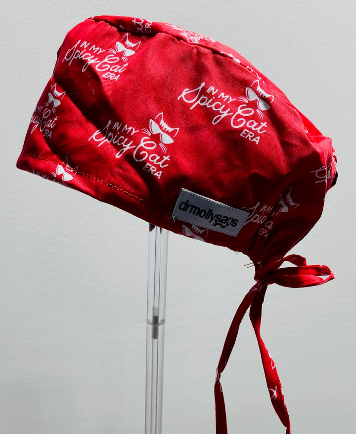Red scrub cap with 'In My Spicy Cat Era' text on a gray background
