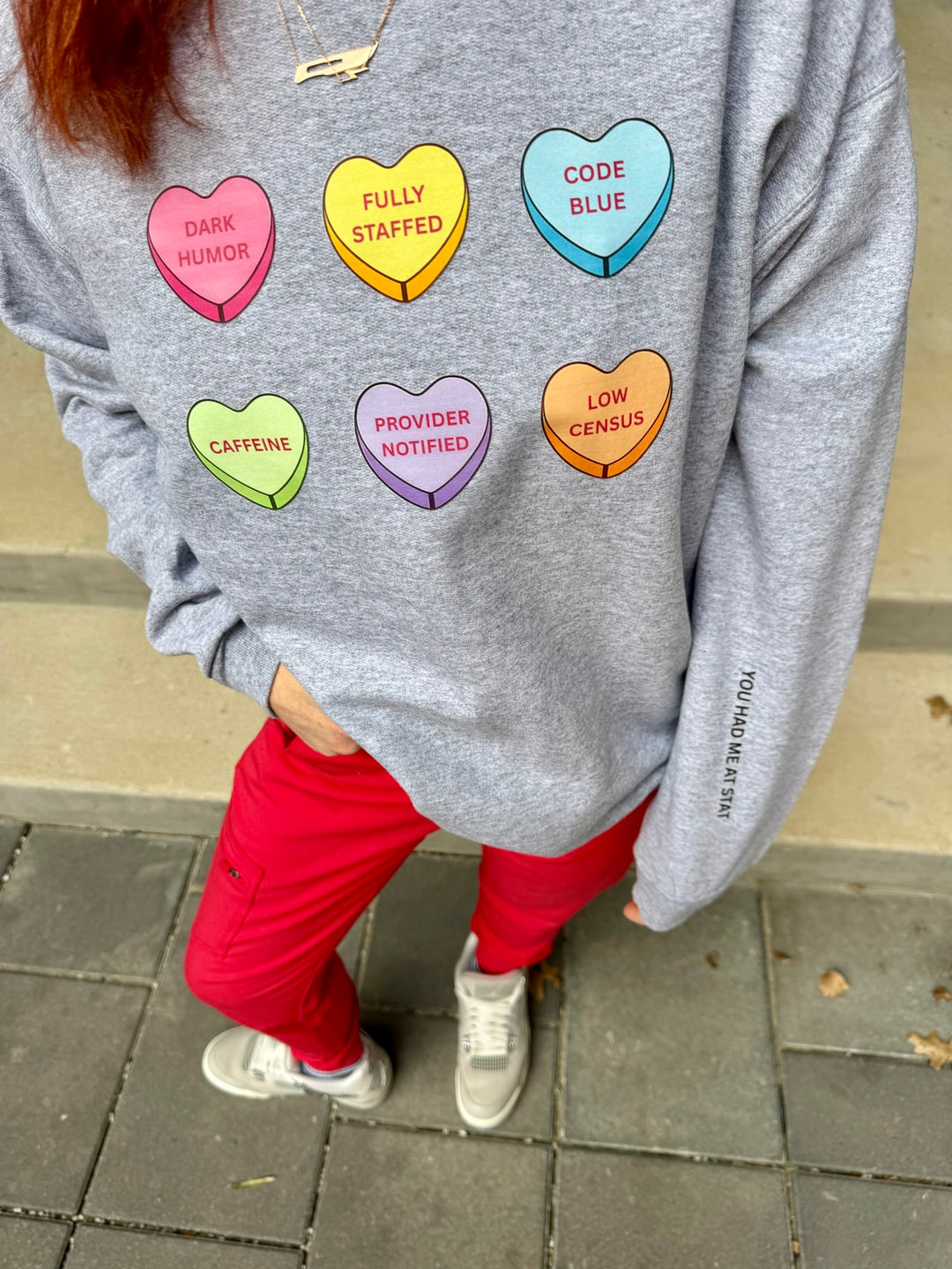 Ladyspinedoc wearing a gray sweatshirt with colorful heart-shaped text designs on a pavement background