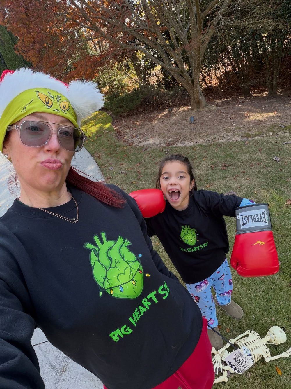 Two people outdoors, one wearing a Big Heart Szn black sweatshirt with a heart design, the child in a matching tee.