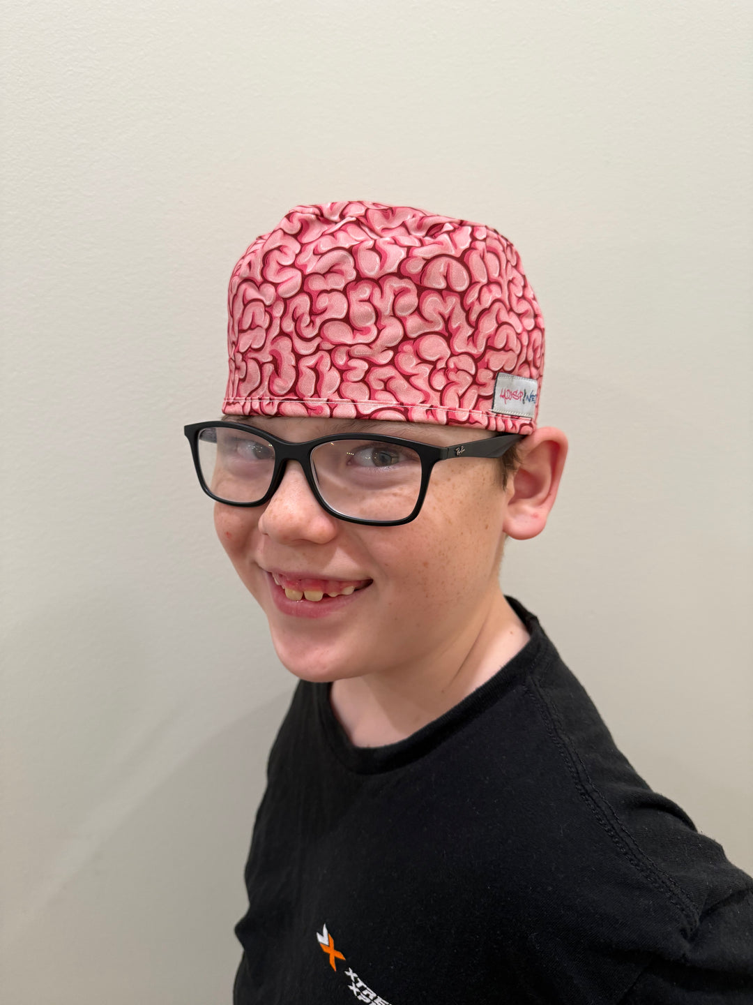 Front view of a youth wearing the tie-back (short hair) version of the Cortex Cap - Pink Scrub Hat with Brain Design