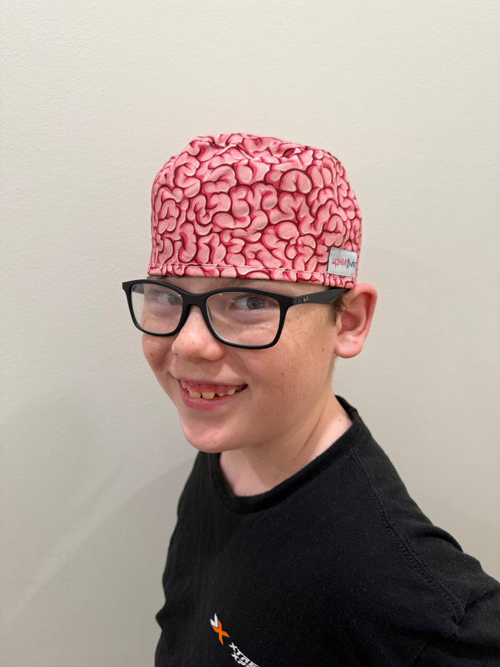Front view of a youth wearing the tie-back (short hair) version of the Cortex Cap - Pink Scrub Hat with Brain Design