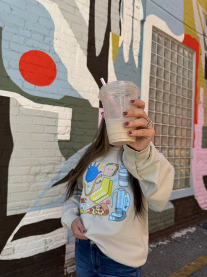 Women hiding her face with a cup and wearing a beige Nurse Sweatshirt with cartoon nurse memorabilia on the front. 