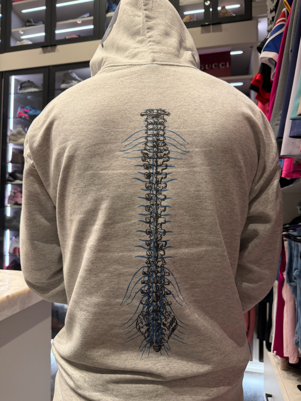 Gray cerebrospinal hoodie with a detailed spine design on the back, worn by Ladyspinedoc in a her home closest.