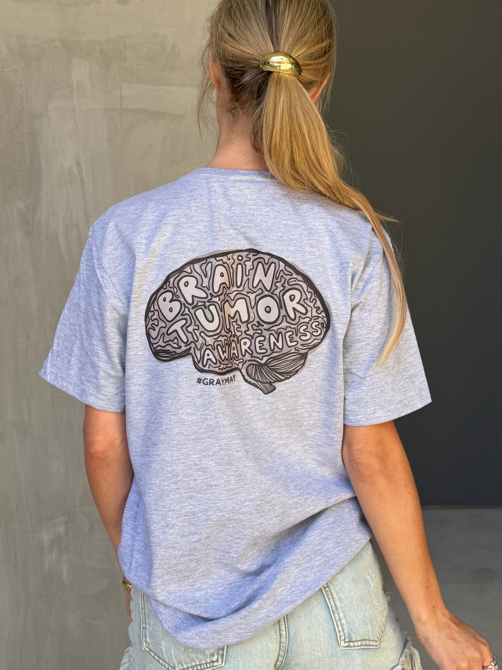 Person wearing a gray t-shirt with 'Brain Tumor Awareness' design on the back.