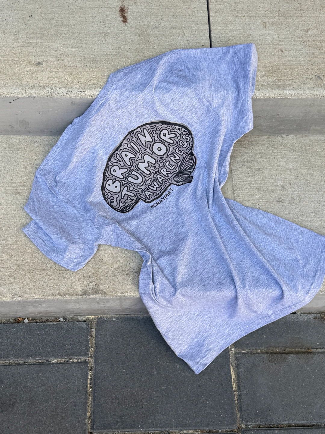 Gray t-shirt with a brain tumor awareness graphic design on a stone surface
