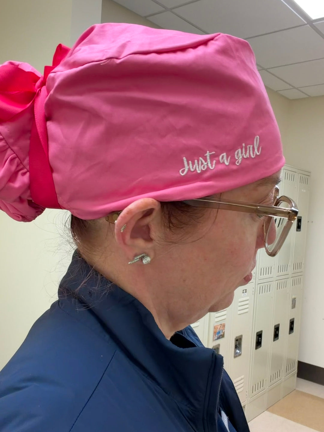Ladyspinedoc wearing a pink scrub cap with 'Just a girl' text in a locker room.