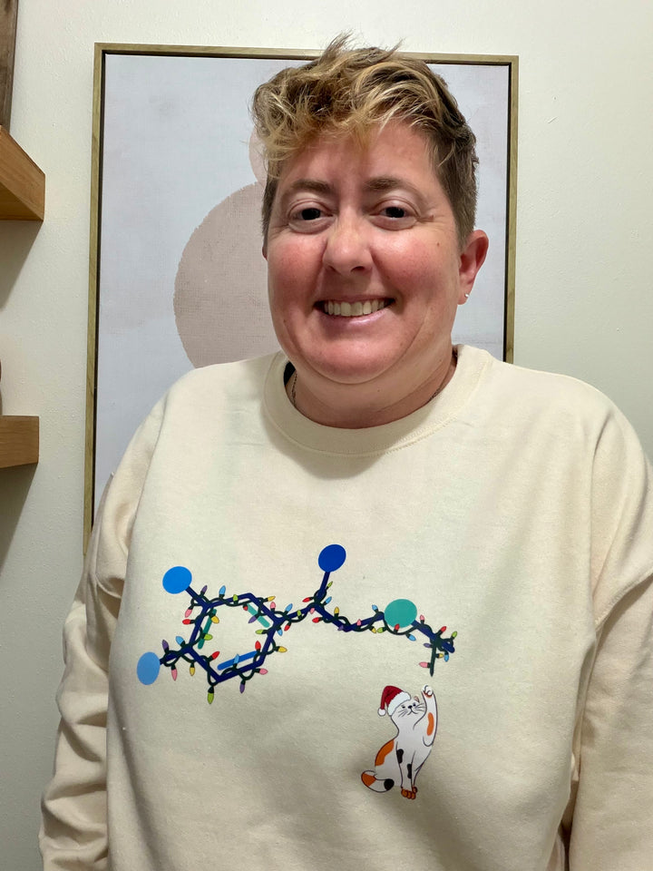 Dr. Beachgem wearing a cream-colored Christmas cat sweatshirt with a colorful adrenaline design and cat with santa hat. 