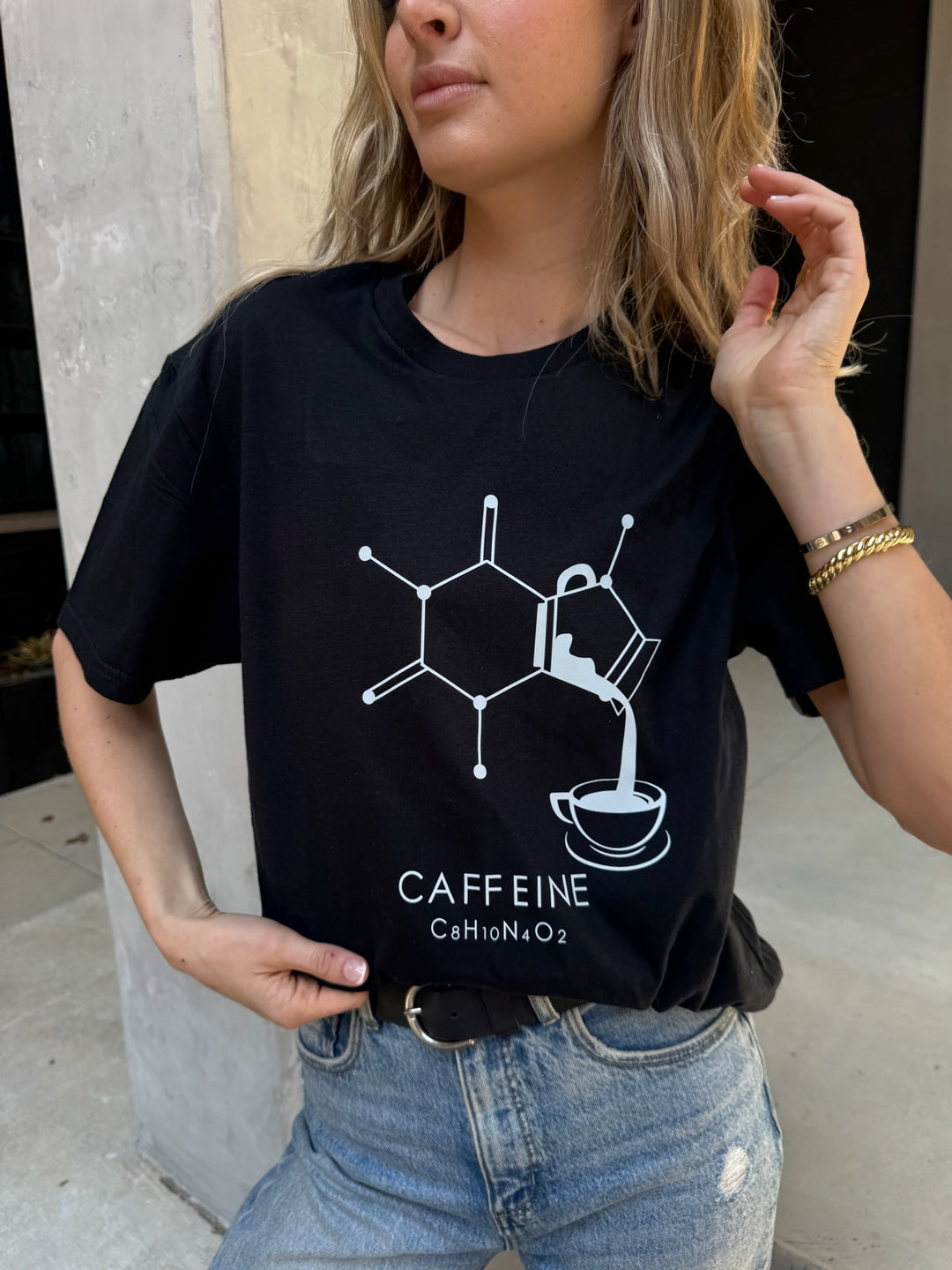 Person wearing a black t-shirt with a caffeine molecule design outdoors.