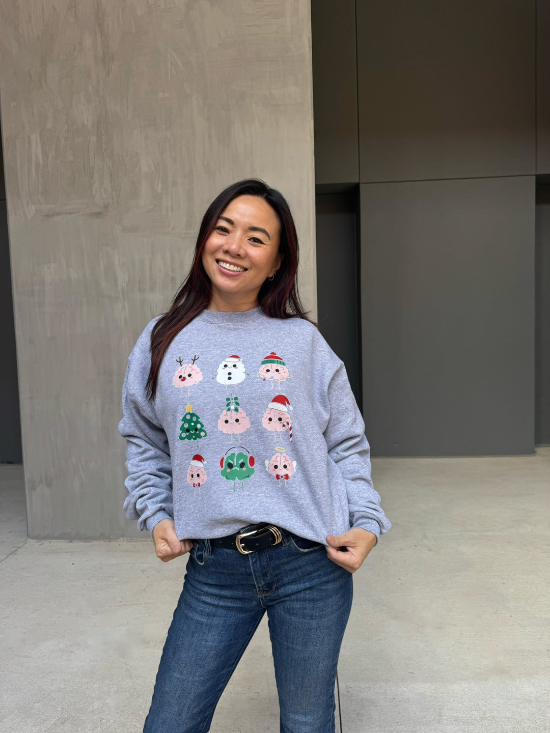 Woman wearing a gray sweatshirt with Christmas-themed brain designs, standing against a plain background.