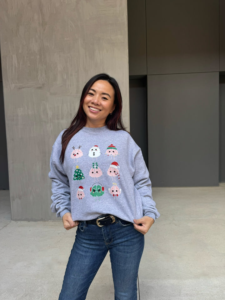 Woman wearing a gray sweatshirt with Christmas-themed brain designs, standing against a plain background.