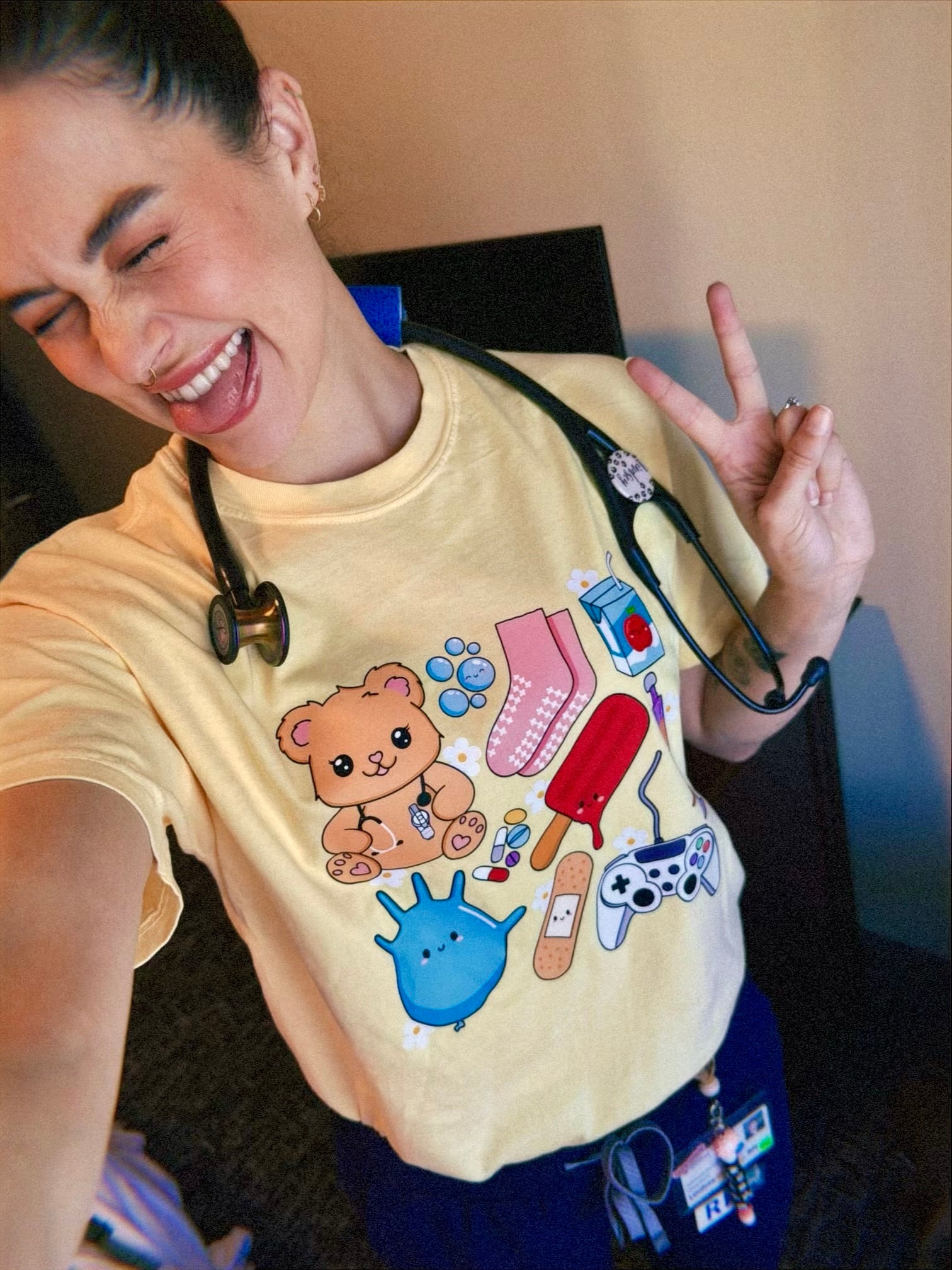 Scrubhacks giving the peace sign and wearing yellow Pediatrics Collage Tee Shirt